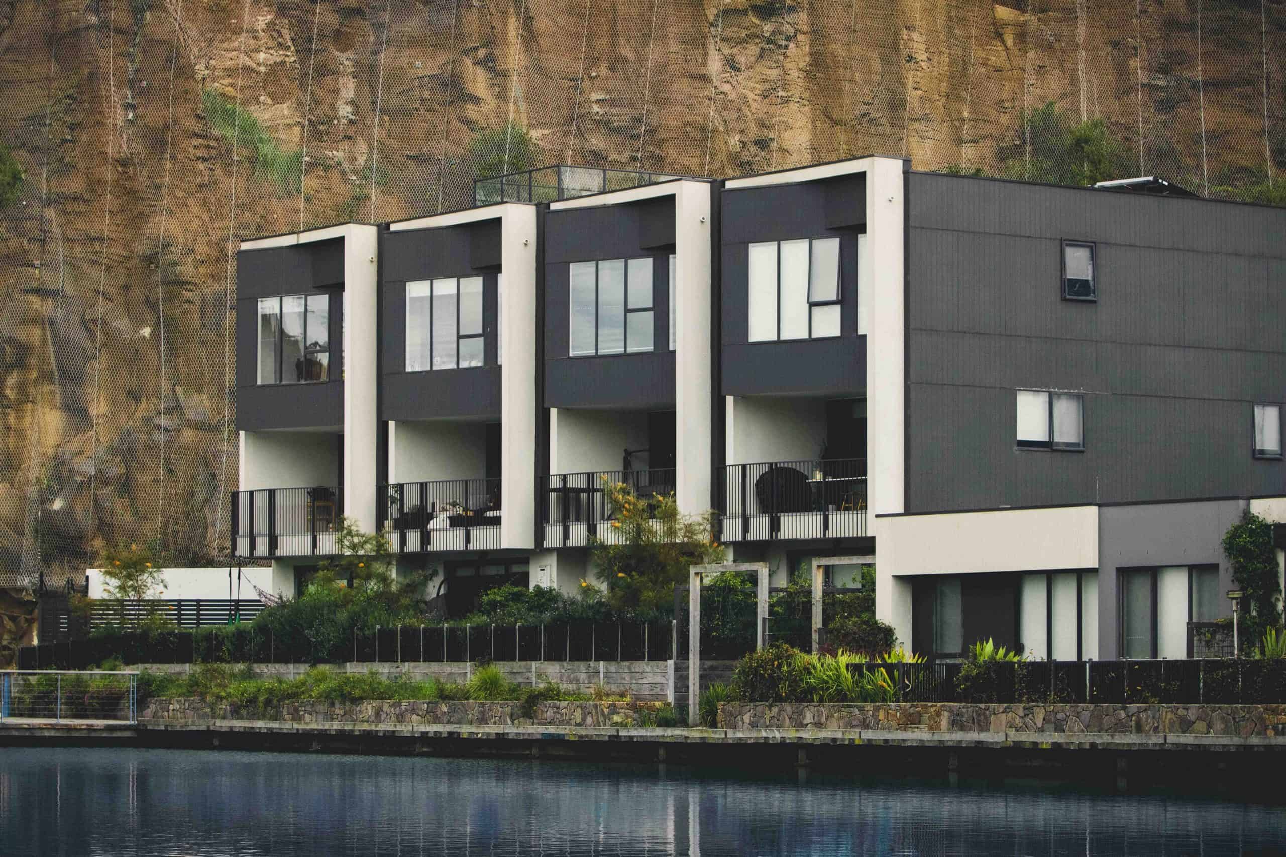 Modern waterfront condominium buildings with balconies below a steep rock cliff.