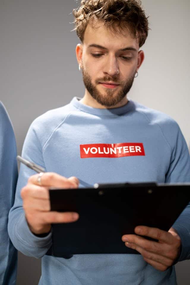 Volunteer in a blue sweatshirt writing on a clipboard, representing organized and manageable community participation.